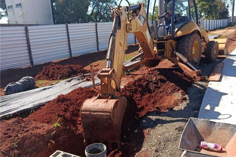 Retroescavadeira abrindo vala de drenagem ao lado de poço de visita em bloco