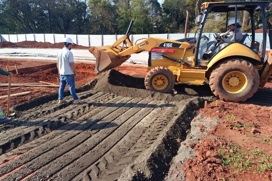 Pá carregadeira espalhando material da base sob acompanhamento técnico