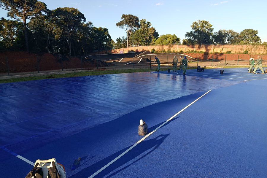 Equipe aplicando camada azul sobre a pista no início da manhã