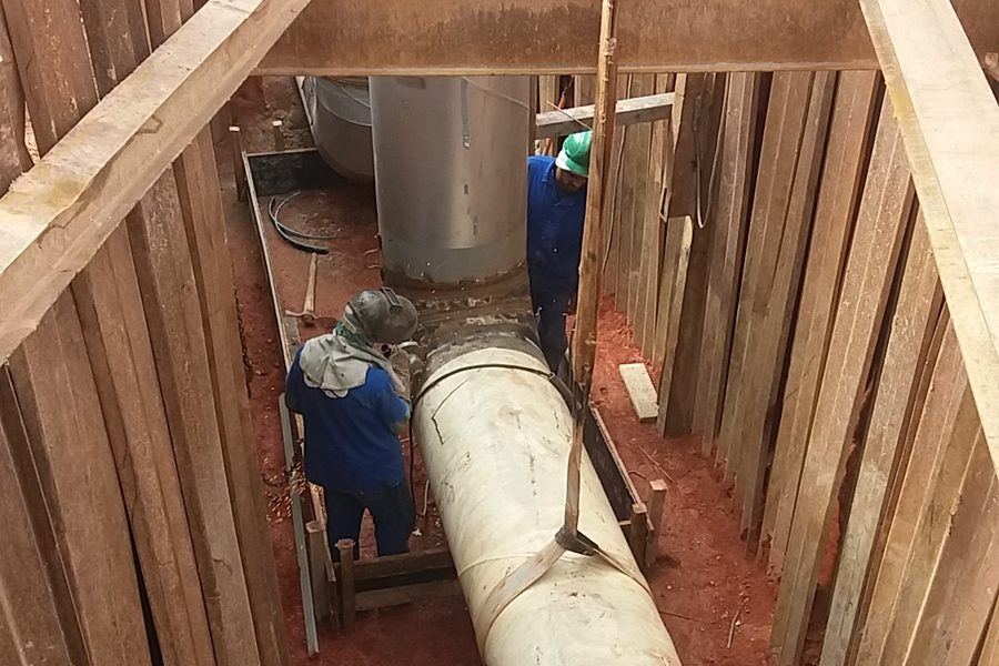 Tubulação sendo instalada em vala profunda com escoramento de madeira