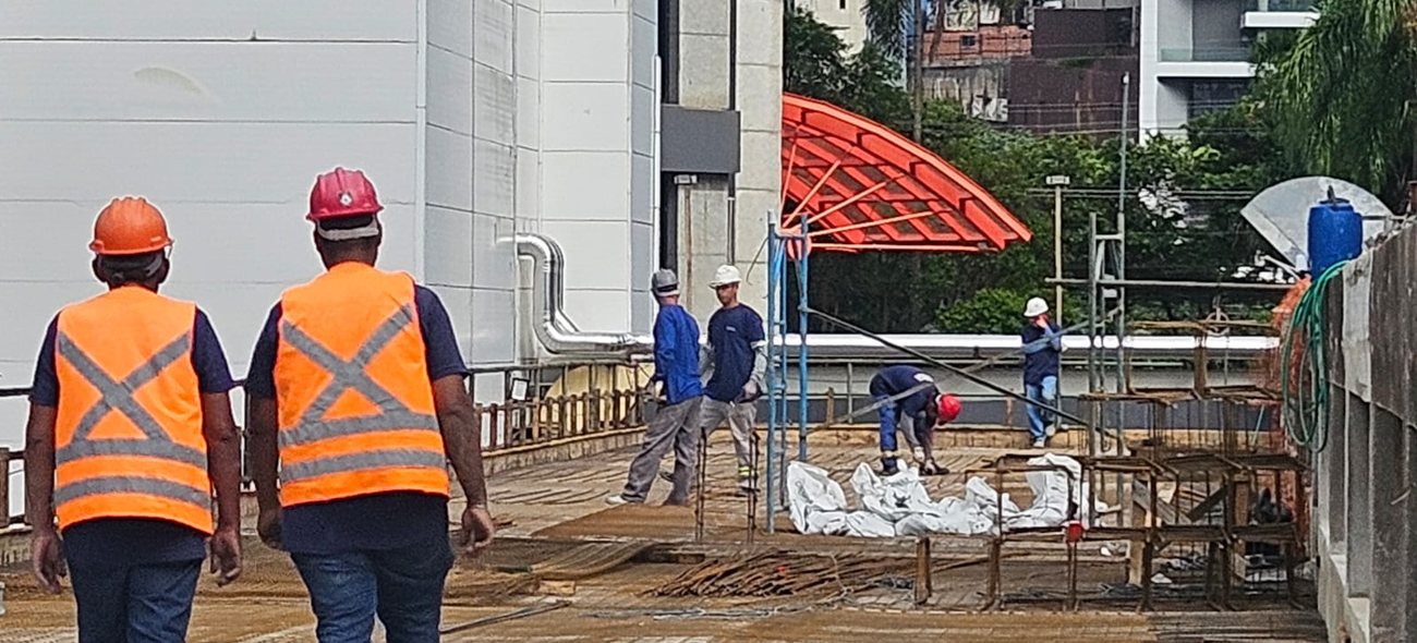 Equipe técnica em EPI atravessando a laje, com frentes de serviço em execução ao fundo