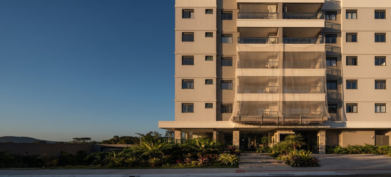 Fachada de condomínio residencial com trecho em reforma, tela de proteção e paisagismo
