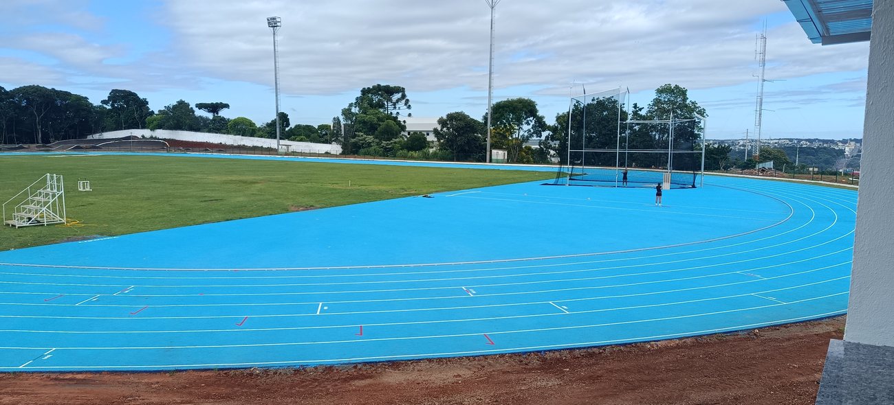 Pista de atletismo azul concluída, com campo e arquibancada ao fundo