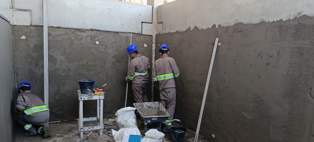 Dois profissionais executando revestimento de parede em obra